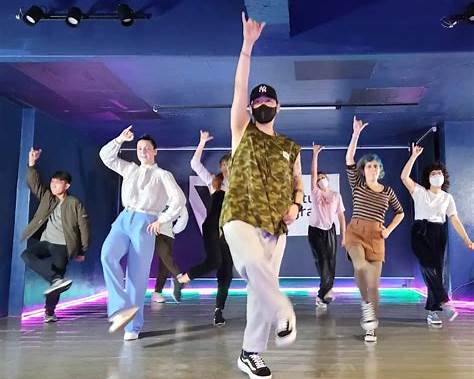 Neon-lit Hongdae-style dance studio with a group practising K-Pop choreography