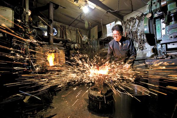A blacksmith working inside a traditional forge workshop as sparks scatter from the hot metal