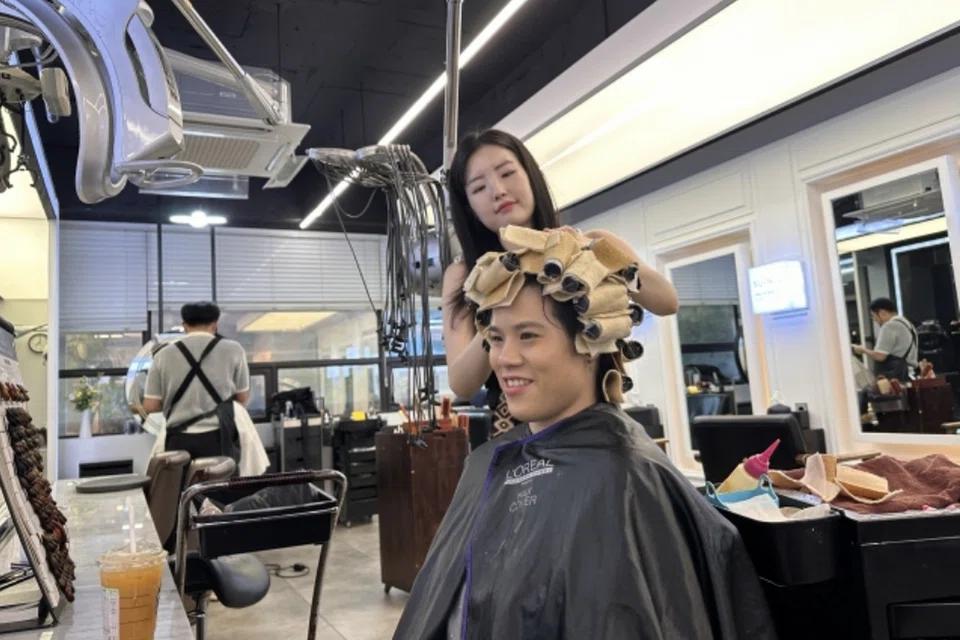 Korean stylist setting a customer's hair with perm rollers under a heat-perm machine
