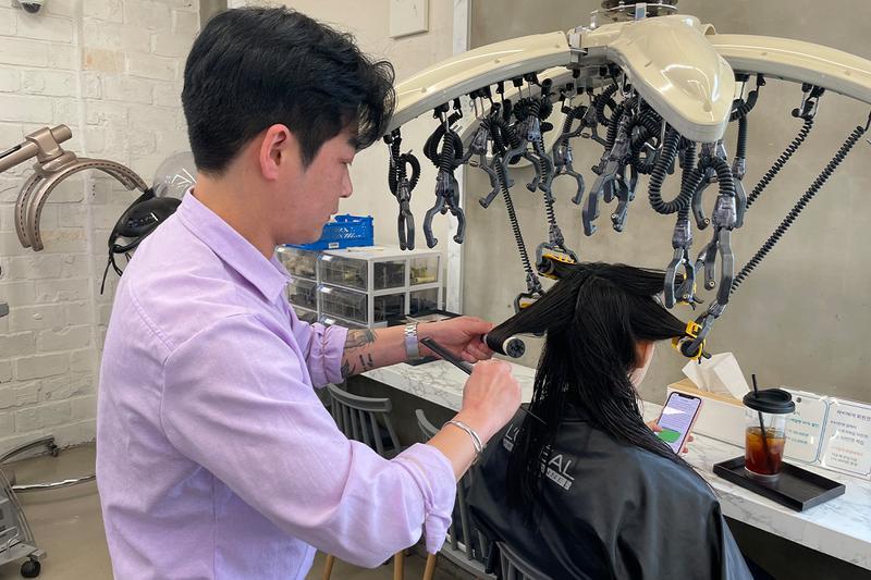 Korean stylist winding a section of hair onto a heated rod beneath a digital perm machine