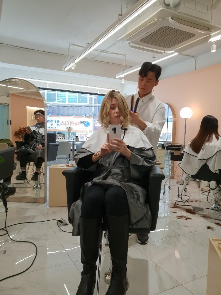 International visitor seated in a bright Seoul salon chair while a Korean stylist cuts and styles her hair