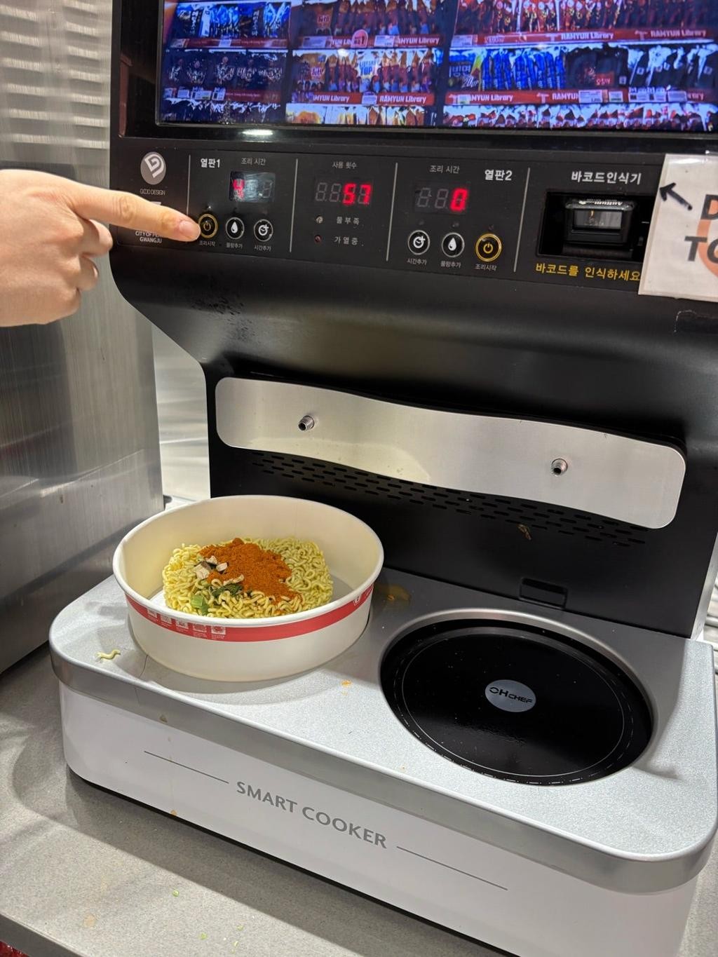 A hand pressing a button on a Korean convenience-store ramyeon smart cooker machine