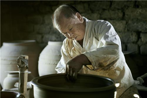 A master Korean potter shaping a large clay jar on a pottery wheel