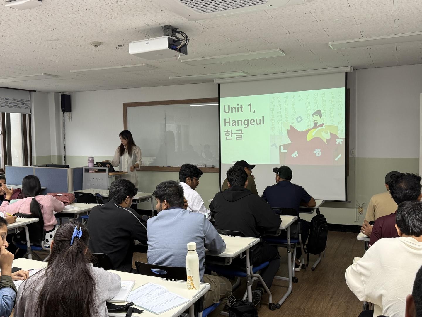 A classroom setting with a projector screen displaying "Unit 1, Hangeul"