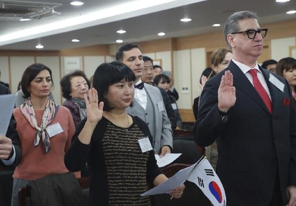 A group of people in a room, some with their hands raised, taking an oath at a Korean naturalization ceremony.