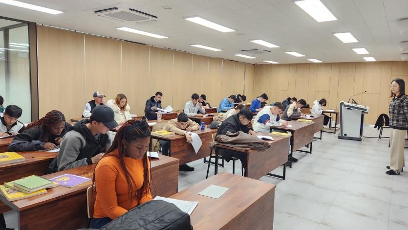 A classroom with students sitting at desks working on papers while an instructor stands at the front.