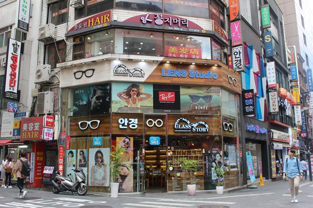 Optical shop storefront with glasses and sunglasses signage on a busy Seoul shopping street