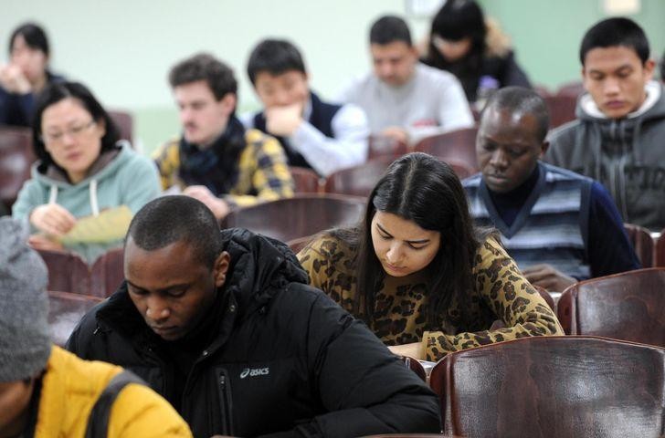 A group of diverse students sitting in a classroom setting, focused on their work.