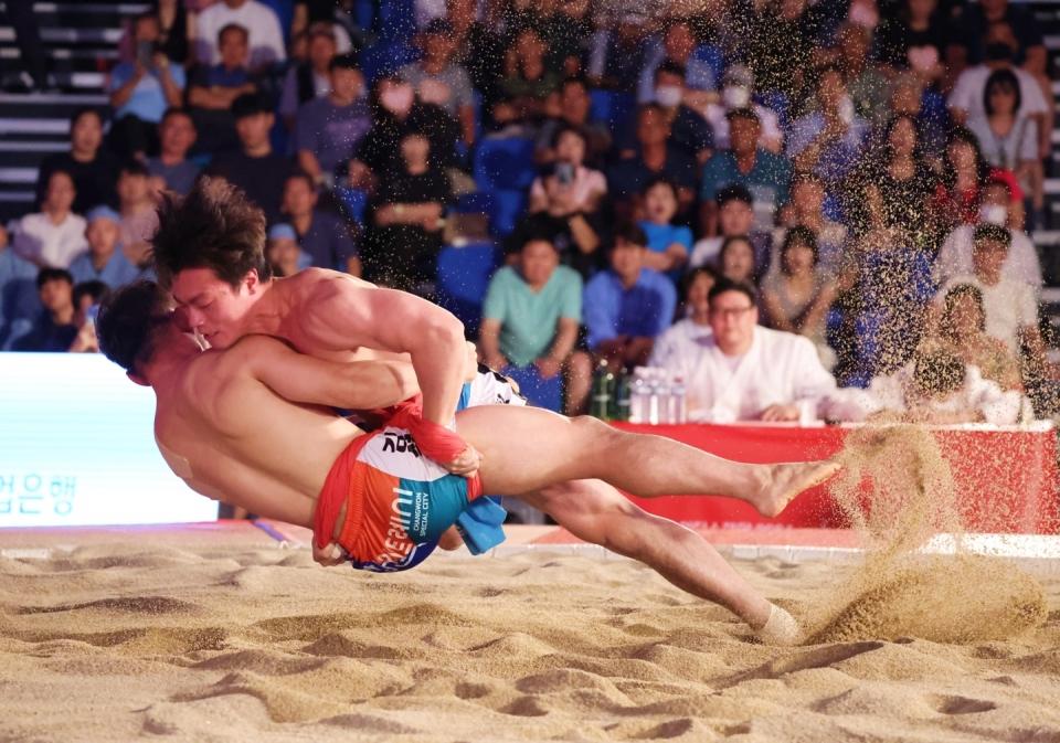 Two ssireum wrestlers gripping each other's satba during a match in the sand ring