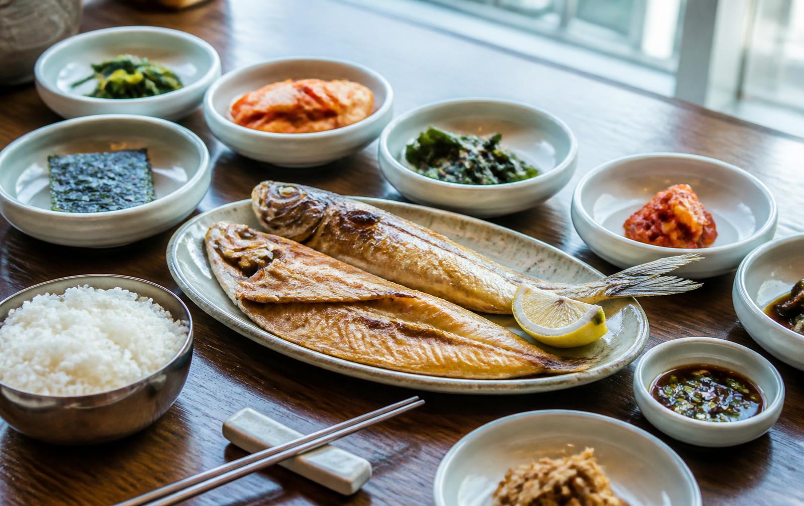 Korean regional meal of soup, rice and many small banchan side dishes on a worn wooden table