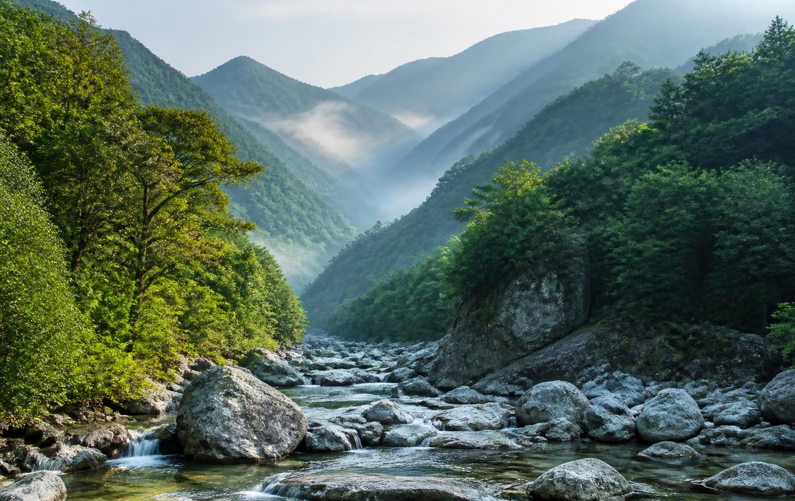 Quiet Korean rural mountain valley with terraced fields, a country road and layered forested ridges