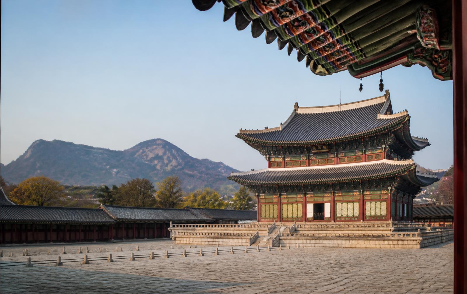 Korean royal palace courtyard in Seoul with painted eaves and mountains behind in morning light