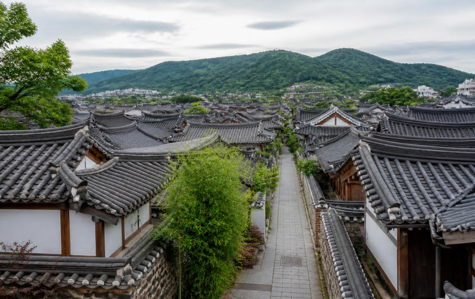 Traditional Korean hanok village rooftops and stone lane with green hills behind