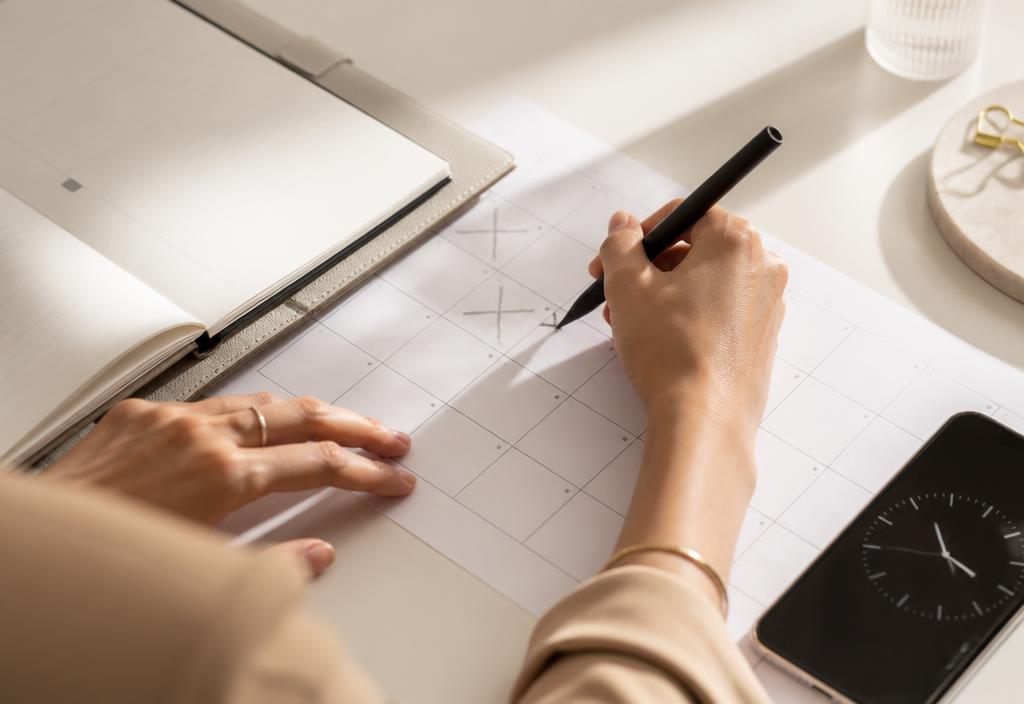 Hands marking travel dates on a paper calendar beside a phone